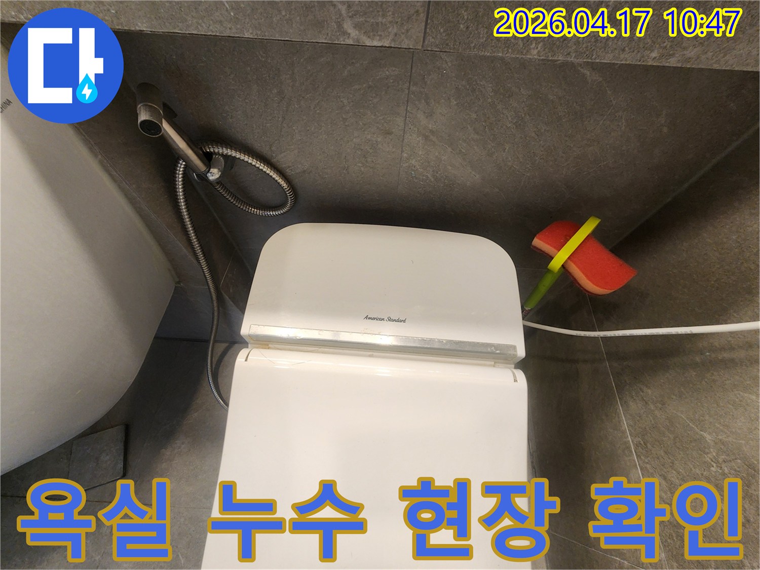 어두운 타일 벽면과-하얀 변기-그리고 청소 도구가 놓인 욕실 전경입니다.
