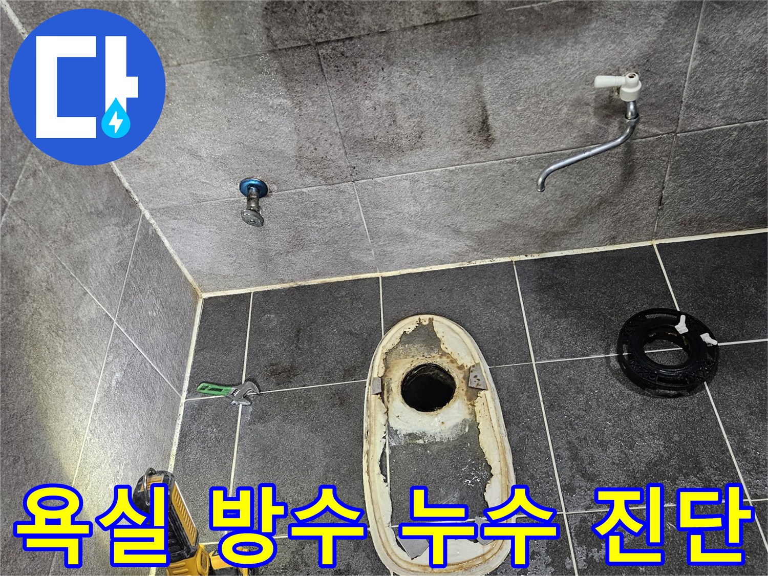 변기가 제거된 욕실 바닥의 배수구와-주변 타일에 스며든 물의 흔적을-손전등으로 밝혀 방수 문제로 인한 누수 여부를 진단하는 모습입니다.
