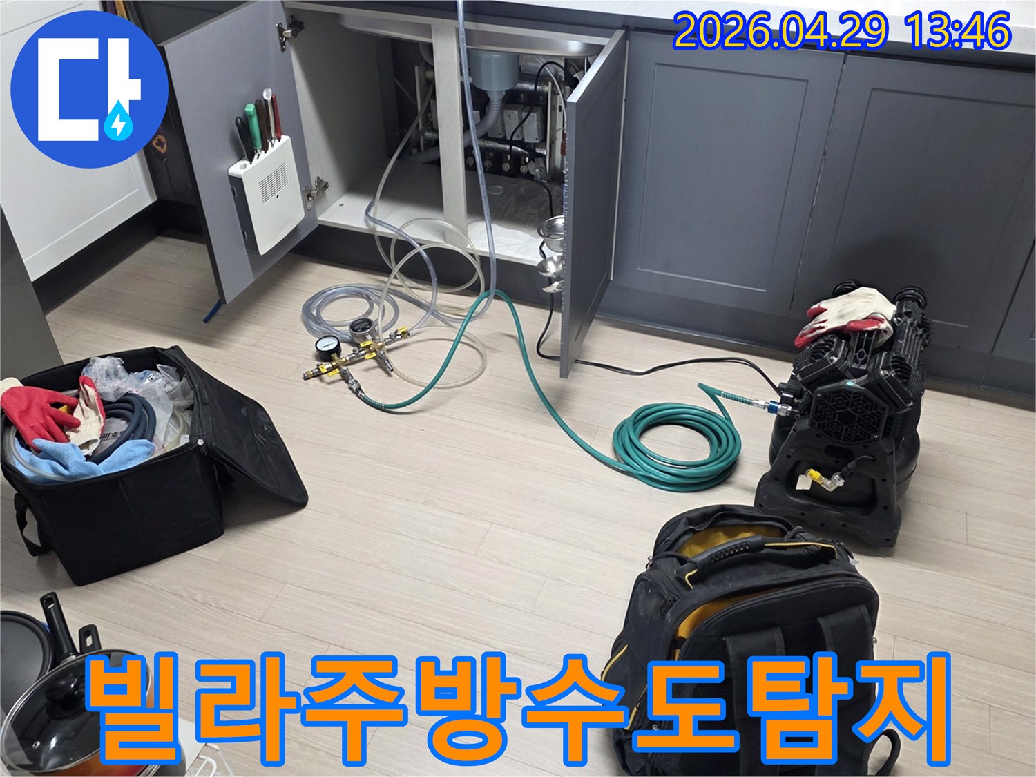 동안구 빌라의 주방 싱크대 하부에서-수도 배관의 누수를 확인하기 위해-압력 게이지와 호스-그리고 공기 압축 장비를-설치하는 작업이 진행 중입니다