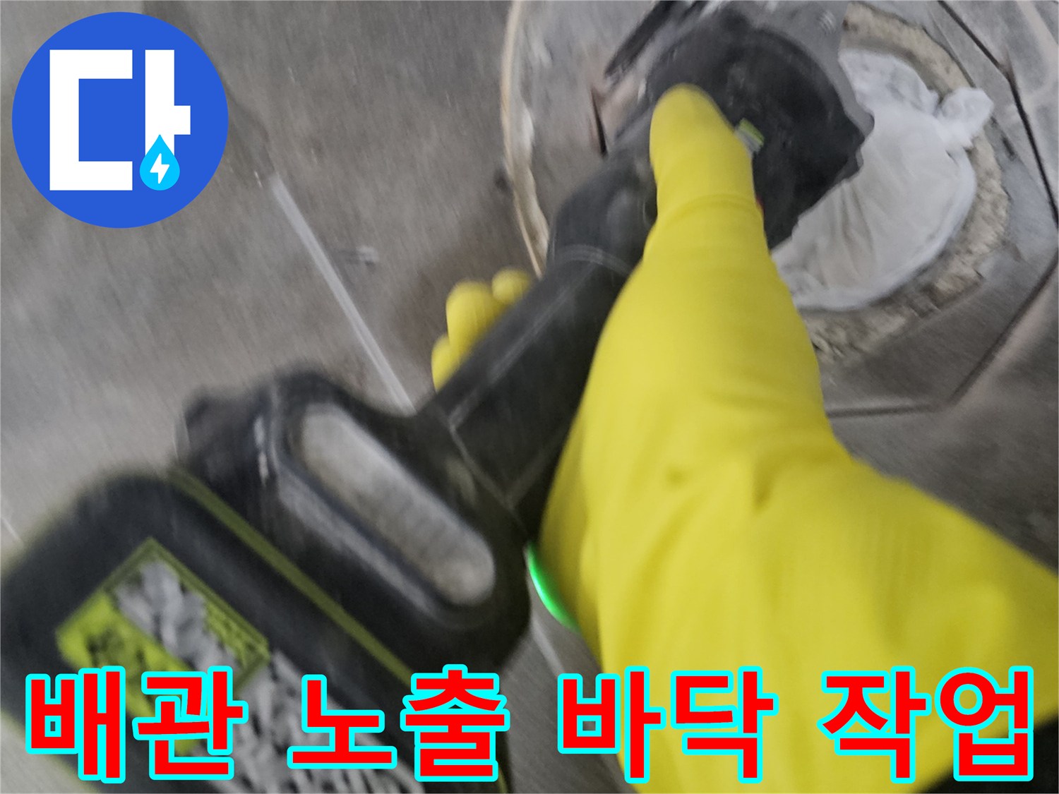 노란색 작업 장갑을 착용한-전문가가-전동 공구로-오수 배관 주변의 바닥 타일을-세심하게 제거하여-배관을 노출시키는 과정입니다.