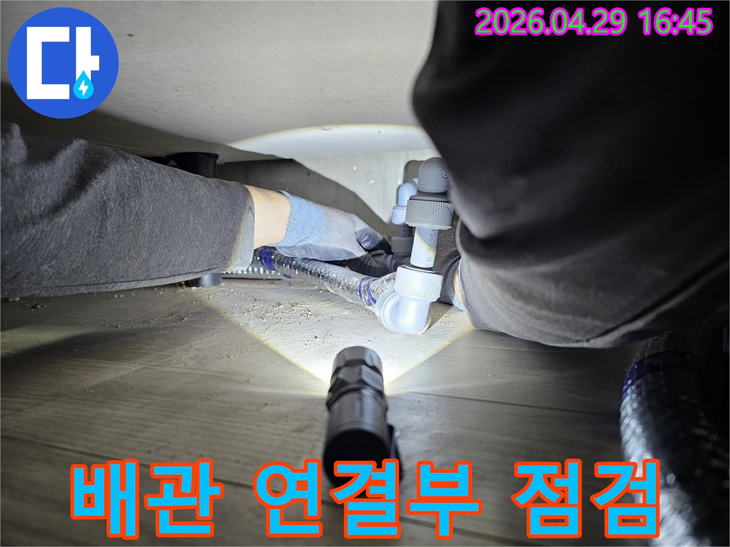 누수-탐지-전문가가-손전등을-사용하여-어두운-배관-아래를-정밀하게-살피는-장면