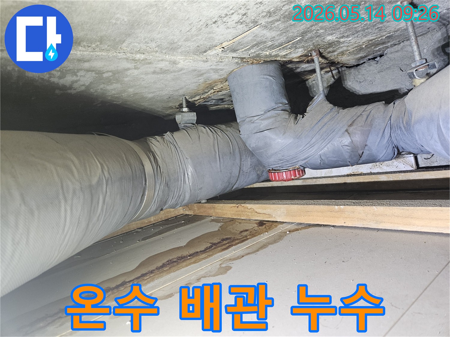 보온재로 감싸진 온수 배관 아래로-물이 스며들어 생긴 넓고 어두운 얼룩이 보이는 천장 모습