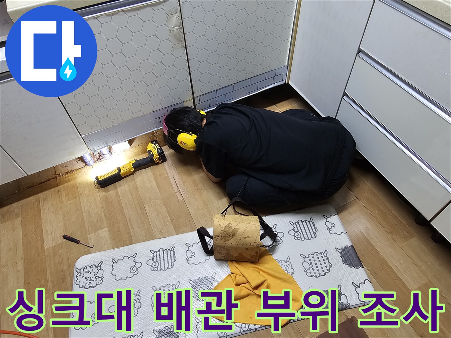 싱크대 아래쪽 어두운 공간에서 조명을 비추어 배관을 점검하는 모습
