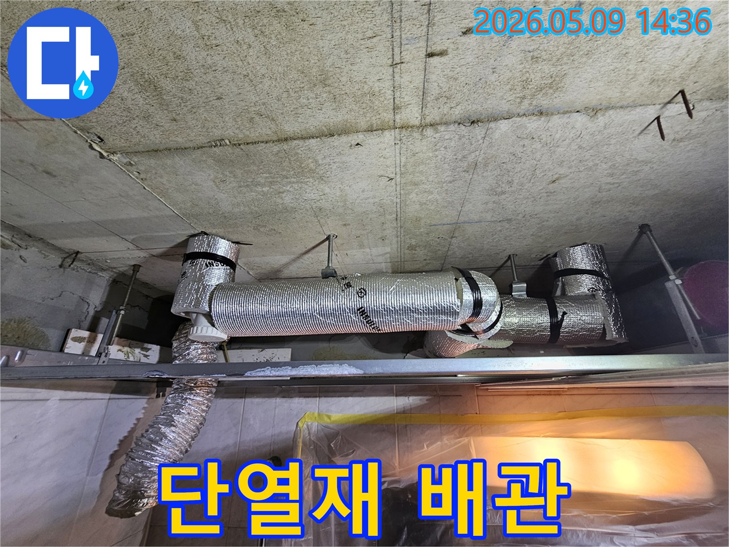 천장 콘크리트 아래에 설치된-단열재로 꼼꼼하게 감싸진 배관의 상태를 점검하는 사진입니다.