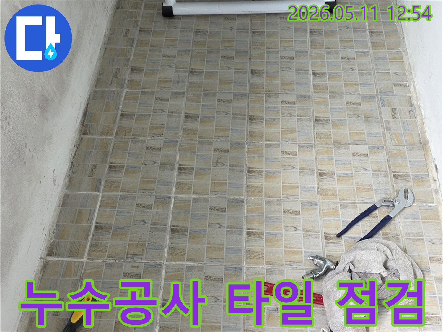 누수 공사 현장에서-타일 벽면과-작업에 필요한 공구들이 놓여있는 모습