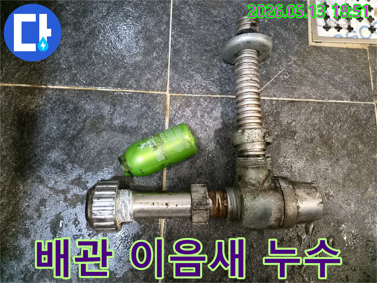 어두운 타일 위에-분리된 배관 이음새 부품과-초록색 샴푸병이 놓여있는-누수 수리 현장 기록