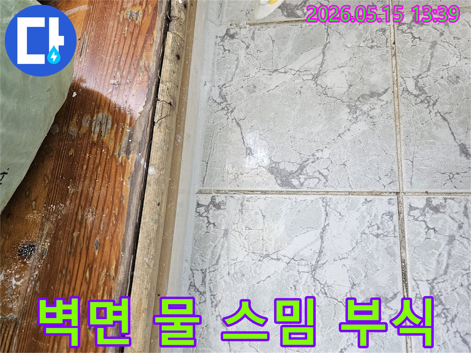 이 이미지는-의정부 신곡동 아파트에서 발생한-벽면 누수로 인해-타일 하단부에 물이 스며들고-목재 마감재가 부식된 모습을 보여줍니다