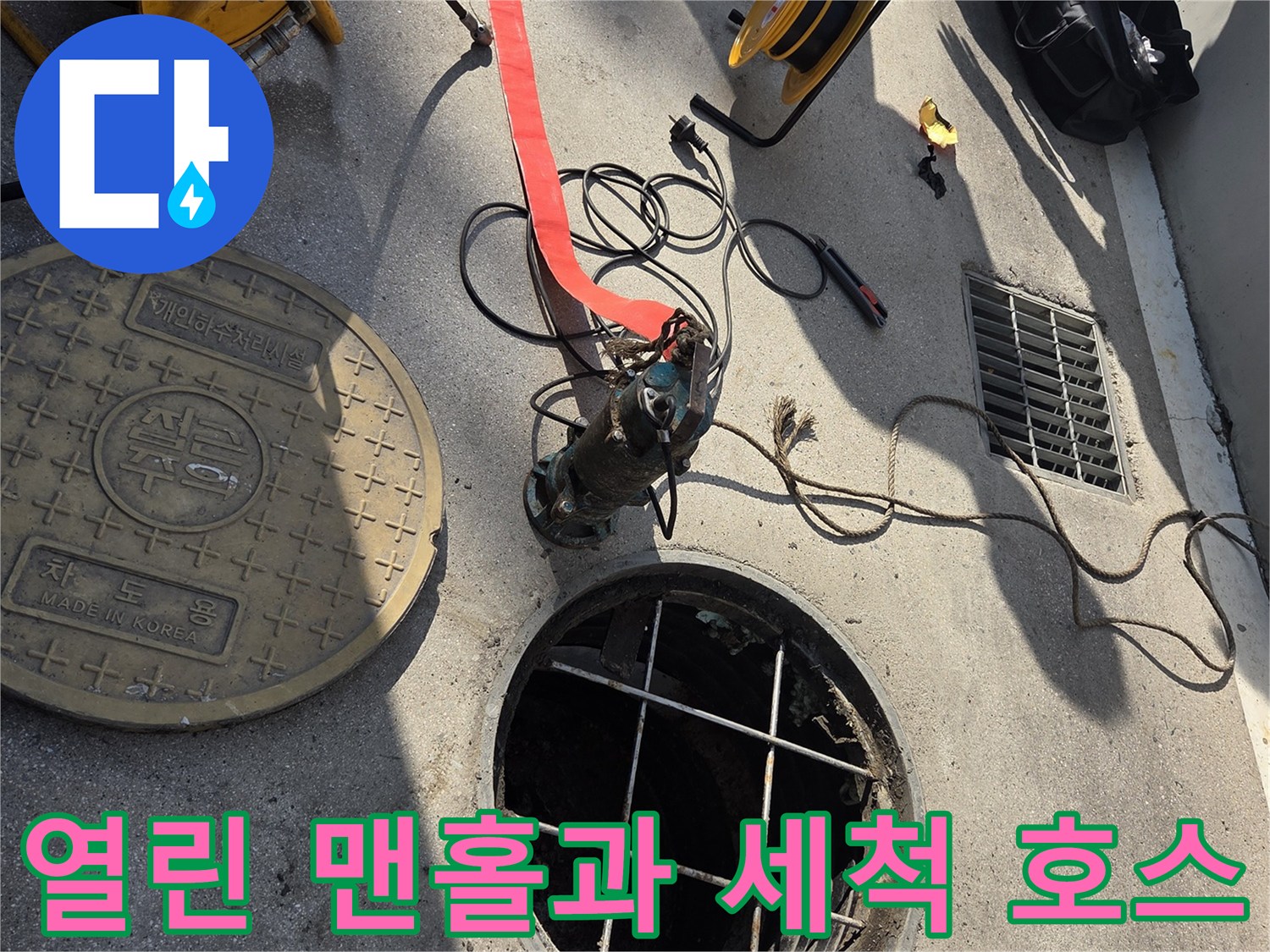 맨홀 뚜껑이 열려 있고 그 옆에 고압 호스가 놓여 있는 현장 사진입니다.