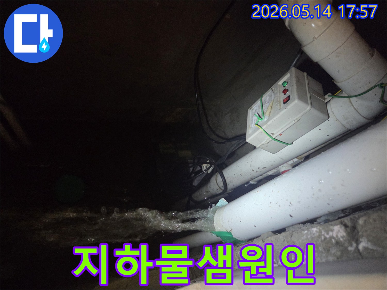 어두운 지하 공간에서-파이프에서 물이 강하게 뿜어져 나오는-물샘 현장을 보여주는 사진입니다-전기 제어 박스와 배관들이 함께 보입니다.