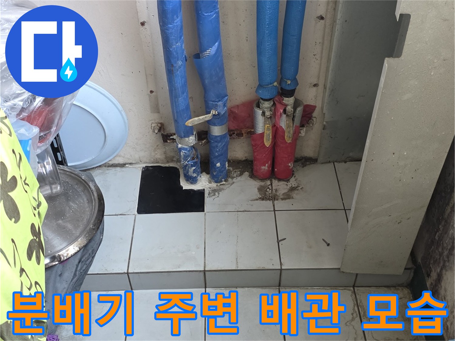싱크대 밑 공간의 파란색 보온재 배관과 타일 벽면이 보이는 사진