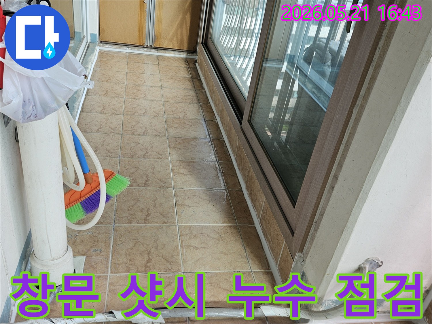 이 이미지는 아파트 베란다의 창문 샷시와-주변 타일 벽면을 보여주며-창문 주변 누수 여부를 정밀 점검하는 현장입니다.