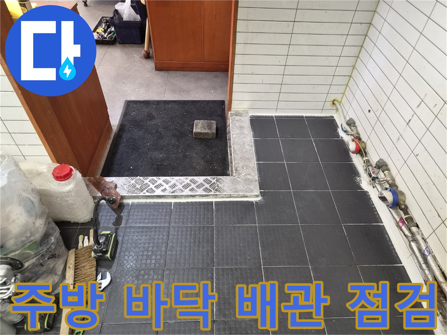 어두운 색 타일과 벽면에 연결된 금속 및 플라스틱 배관 모습입니다.
