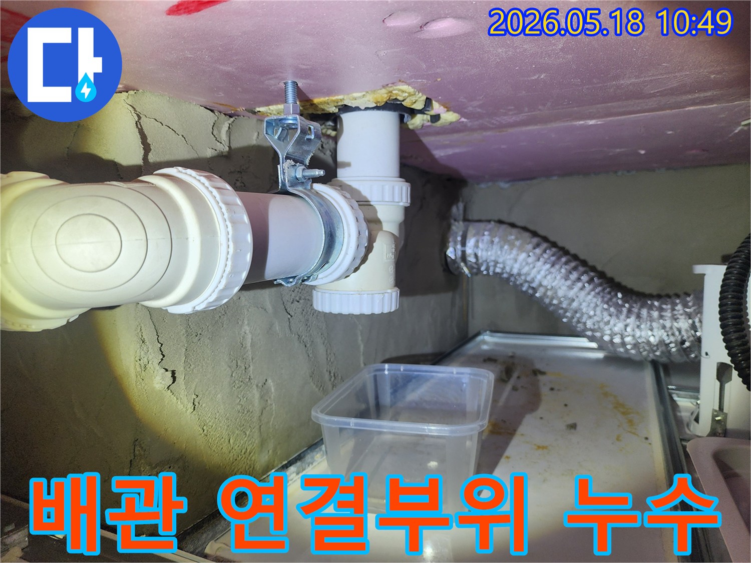 이 사진은 배관 연결 부위에서 물이 새어 나와-임시 용기에 받아지고 있는 현장으로-전문적인 보수가 시급함을 나타냅니다