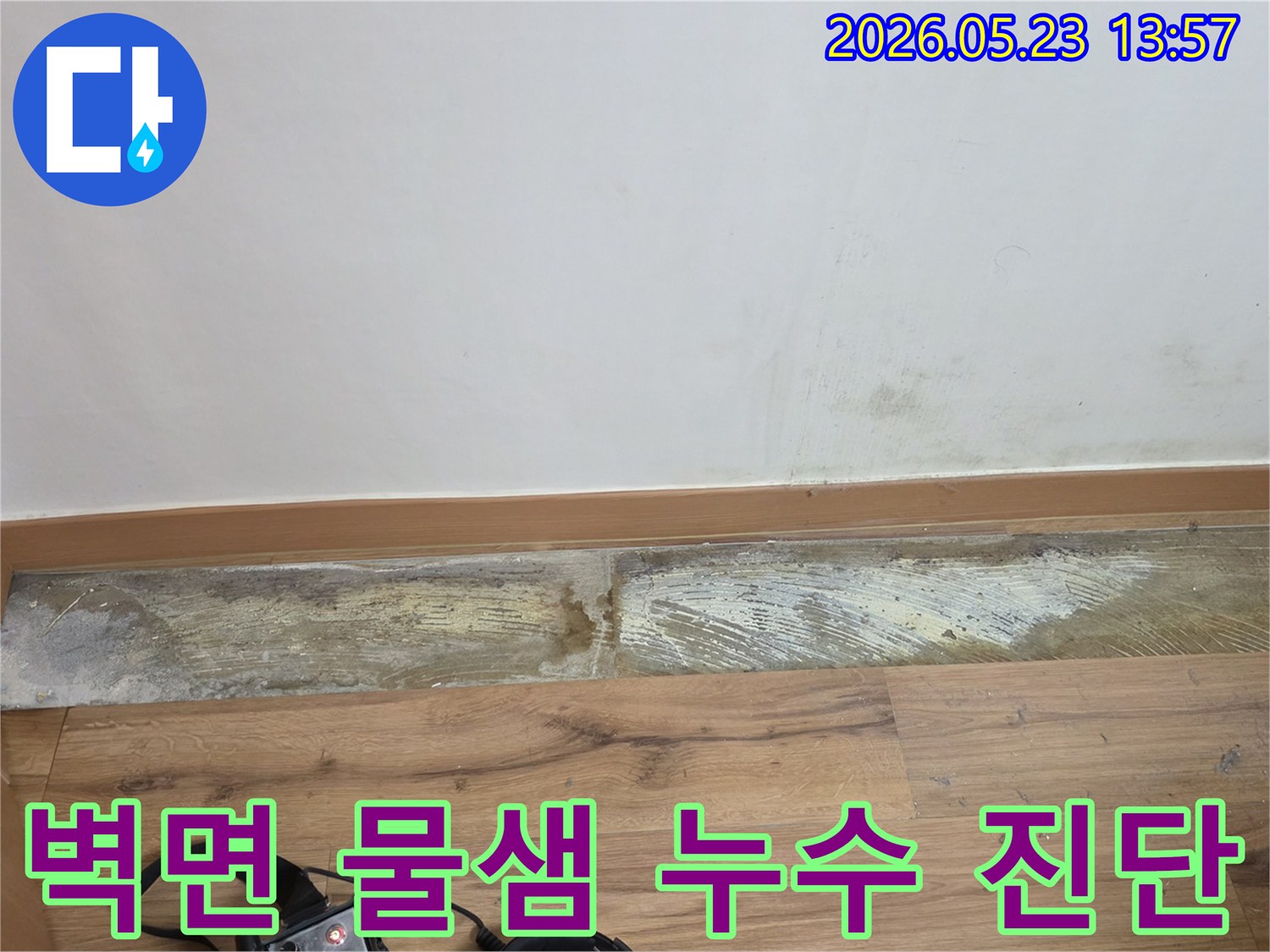 누수 탐지 장비가-바닥에 놓인 채-벽 하단에-발생한-물샘과-습기 흔적을-보여주는-손상된 벽면의-현장 사진