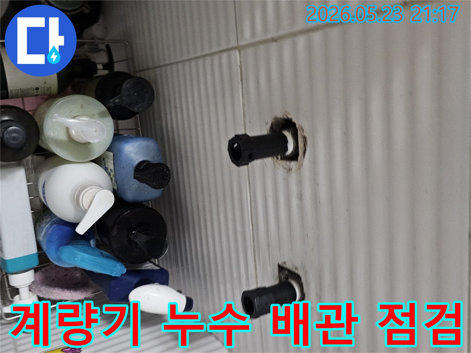 타일 벽면에서 노출된 수도 배관의 연결 부위를-수도 계량기 누수 원인을 찾기 위해-정밀하게 점검하는 모습입니다.