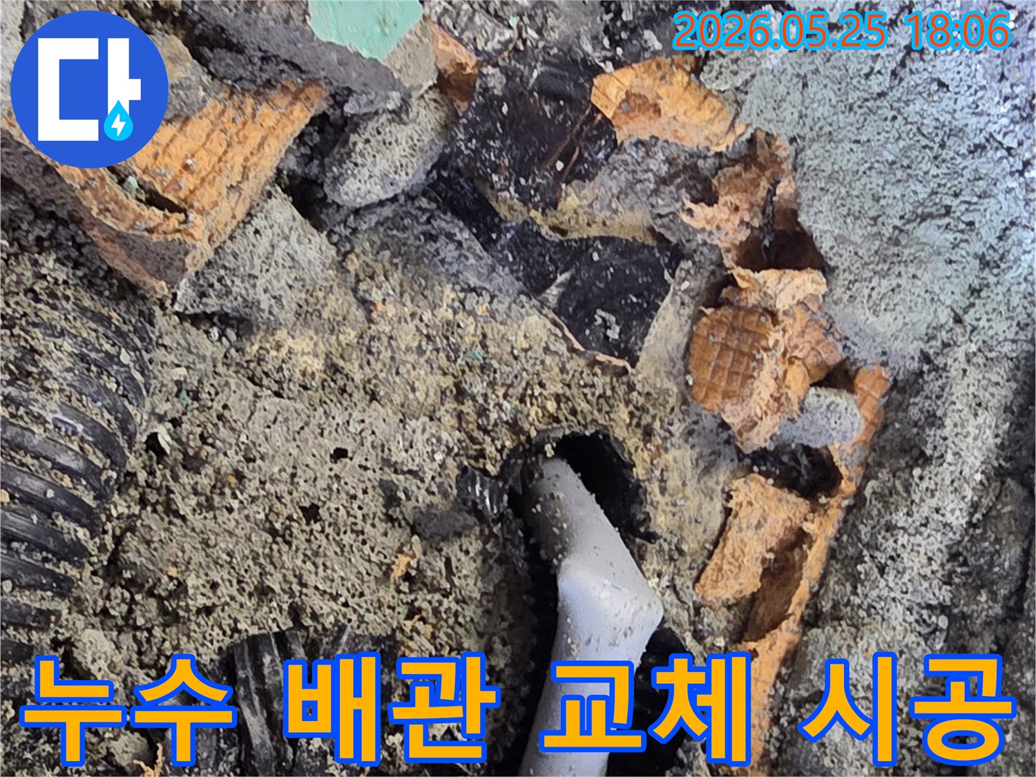 파쇄된 바닥 아래에서 드러난 젖은 배관과 주변의 흙-콘크리트 조각들은-누수 수리를 위한 배관 교체 작업을 보여줍니다.