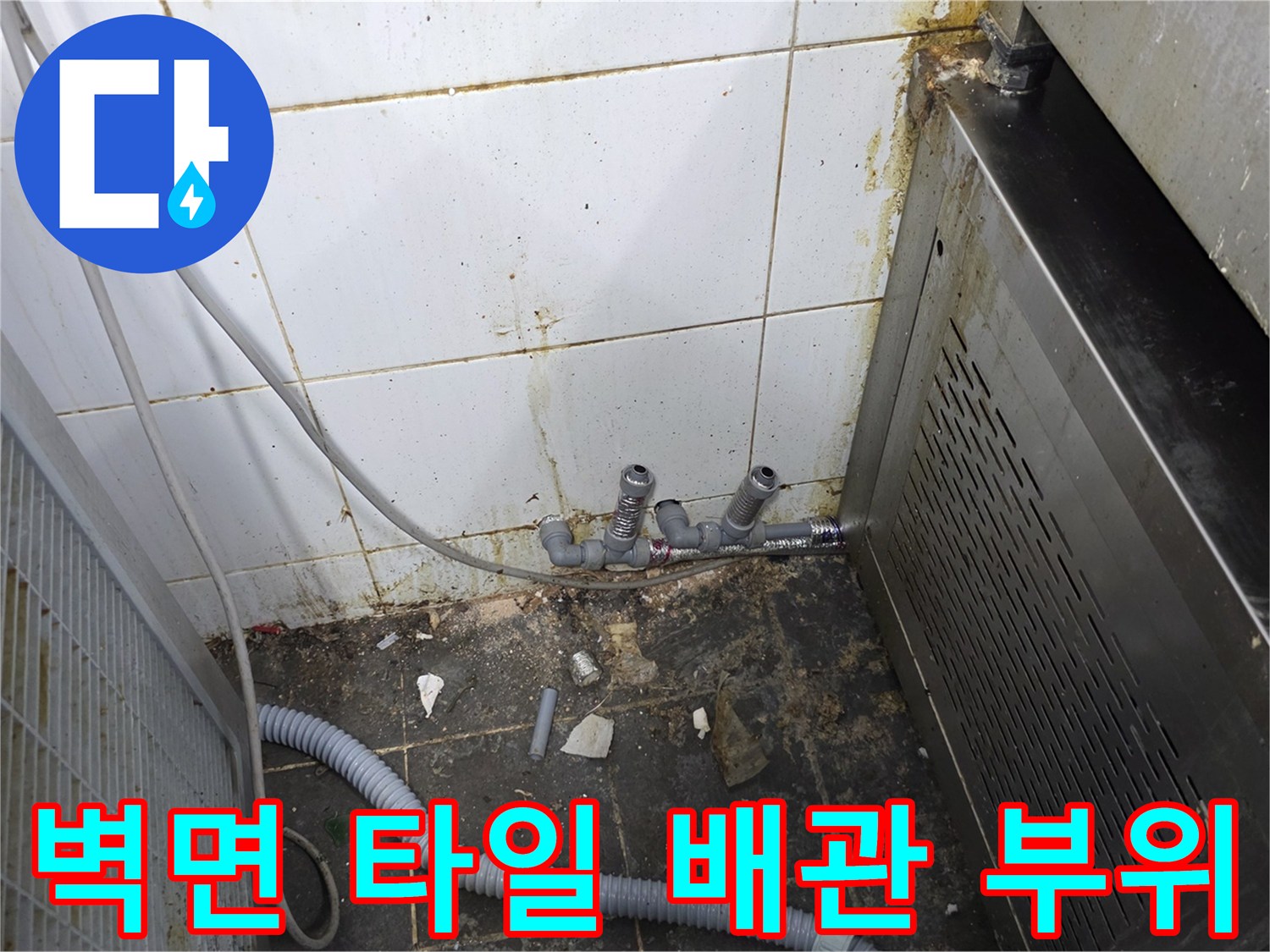 타일 벽면에 노출된 수도 연결 부품과 호스 라인