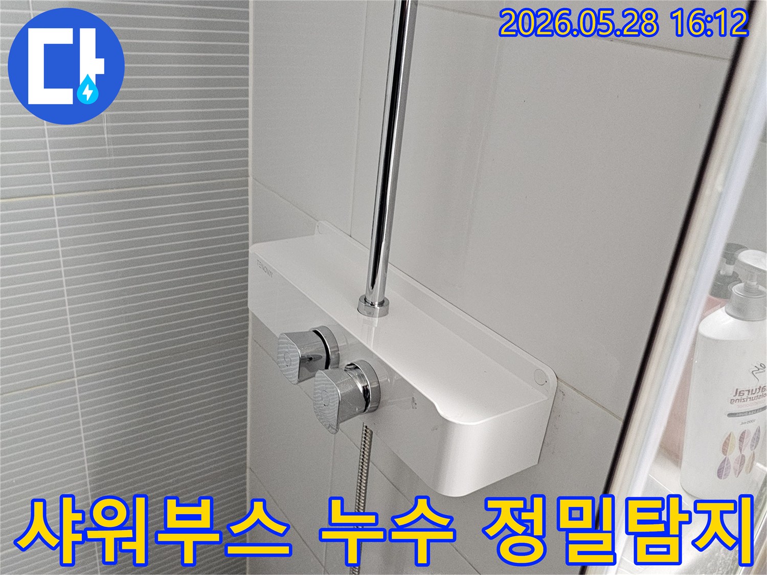 이 사진은-욕실 샤워부스-상단에 설치된-수전과-유리 칸막이-주변을-면밀히-관찰하는-모습입니다.