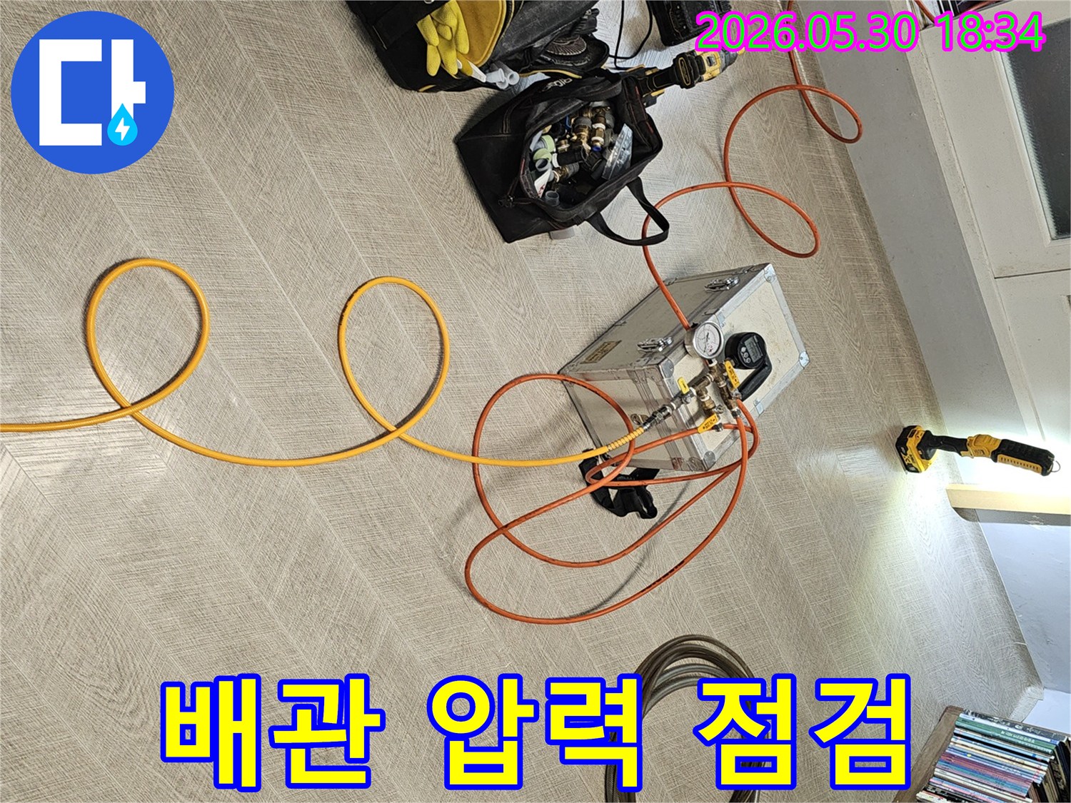 실내 바닥에 설치된 누수 탐지 장비와-다양한 연결 호스-그리고 작업 도구들이-누수 진단을 위해 준비된 장면입니다.