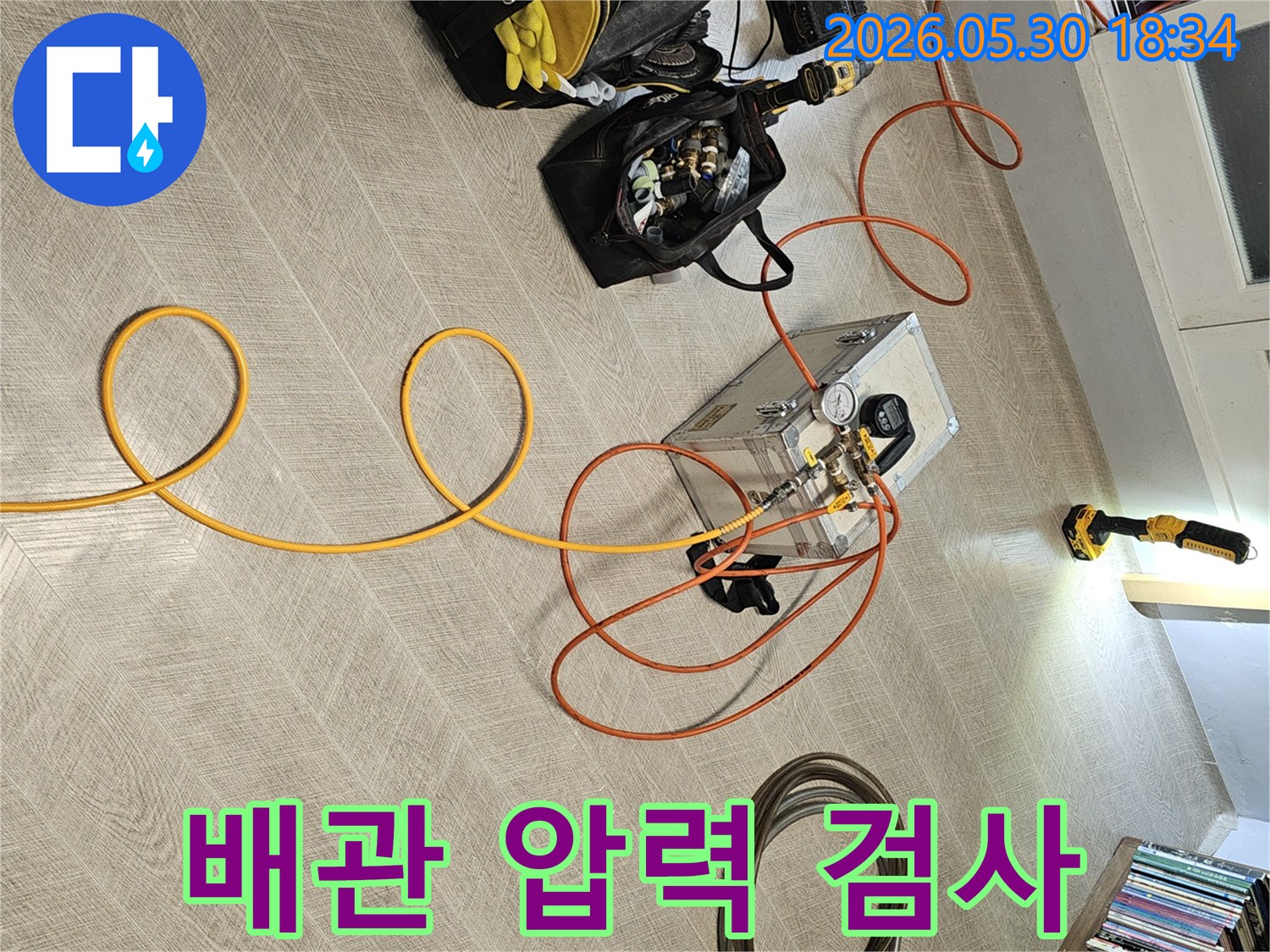 주택 내부에서 누수 지점을 찾기 위해-전문적인 압력 측정 장비와-다양한 연결 호스들이-바닥에 정돈되어 있는 모습입니다.
