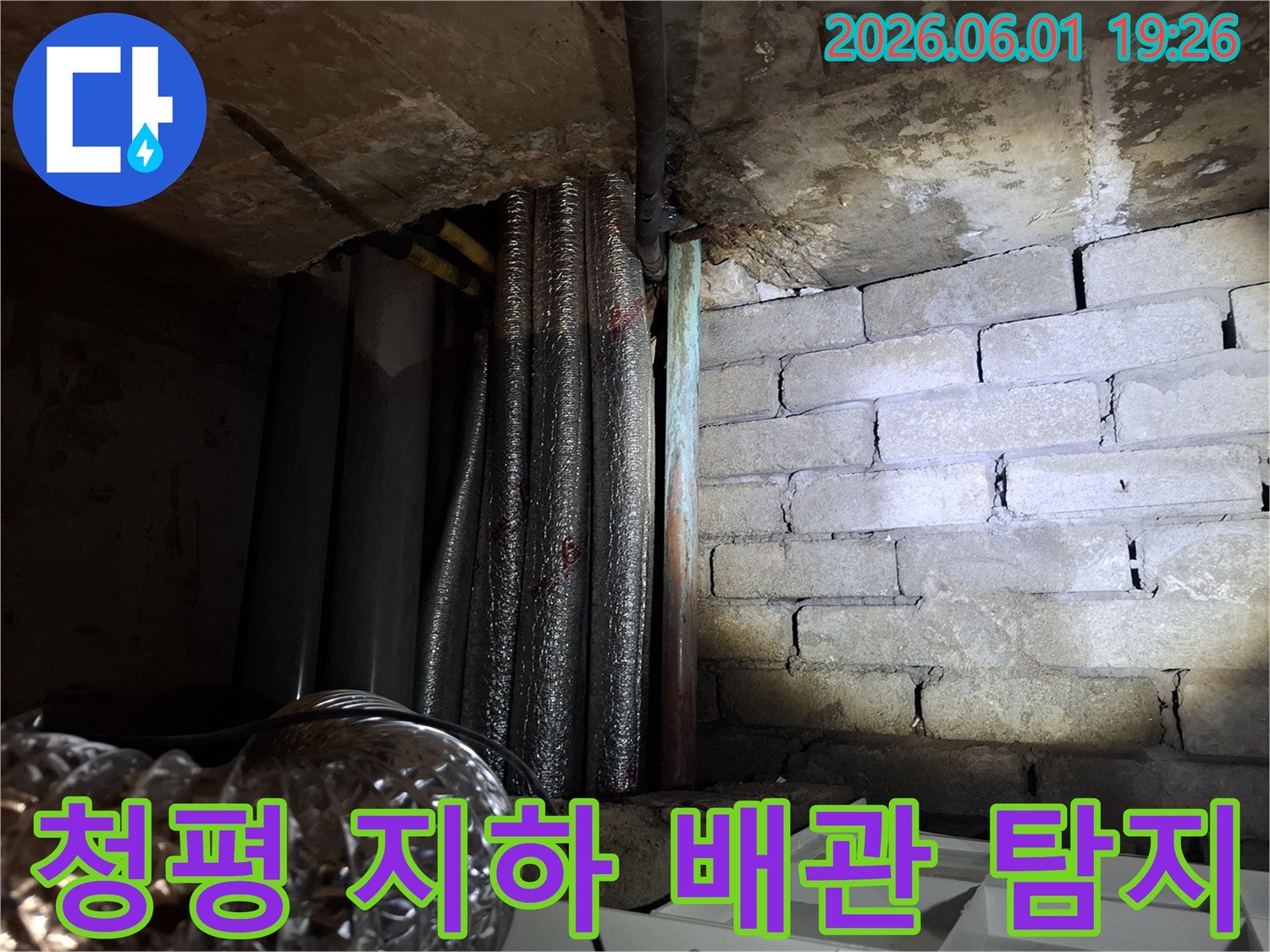 어두운 지하 공간에서-천장 배관과-벽돌 벽면의-젖은 흔적을-확인하는 모습의-누수 현장 사진입니다