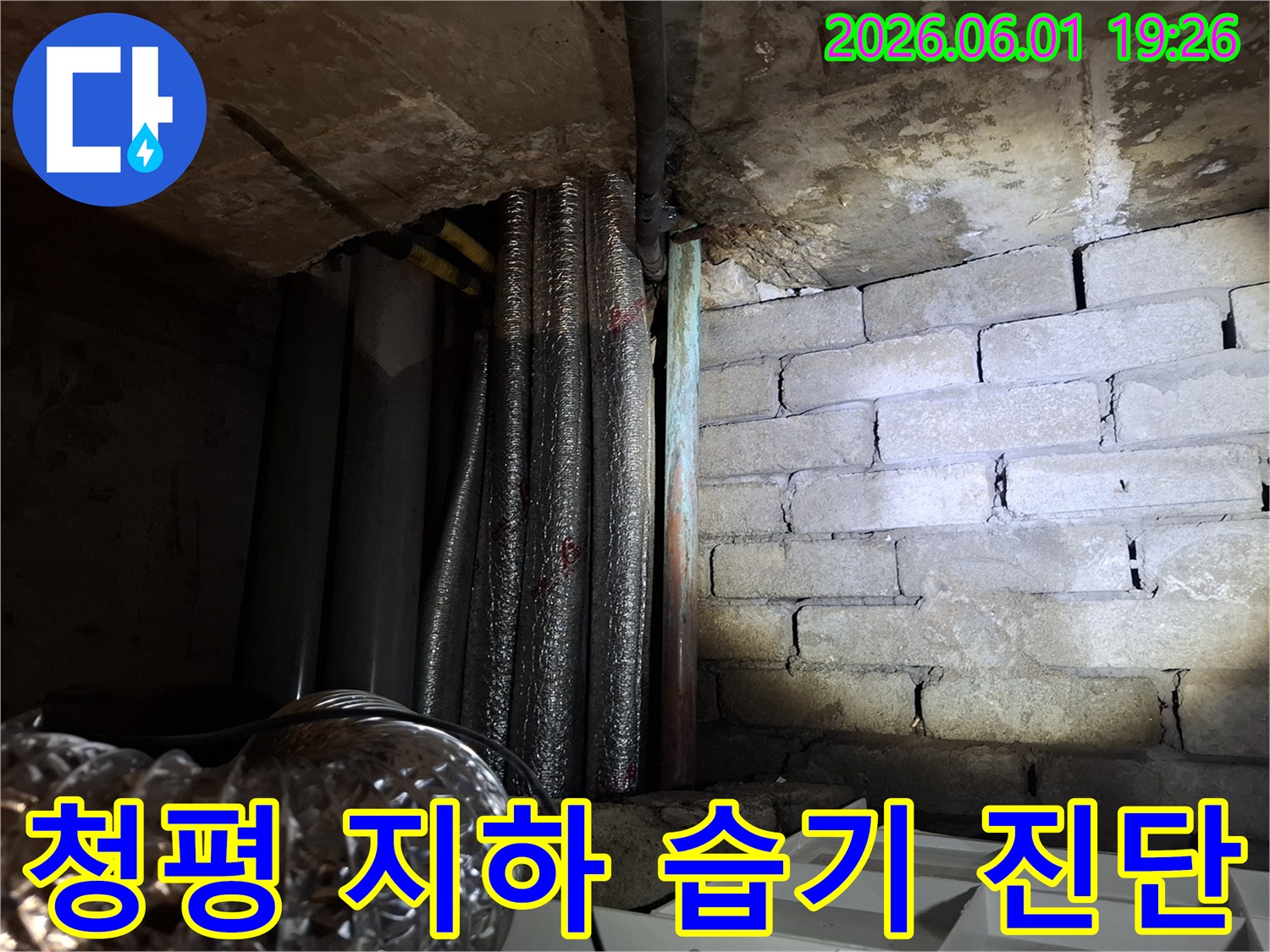 어둡고 습한 지하 공간에서-천장 배관과-벽돌 벽면의-누수 흔적을-확인하는 모습입니다