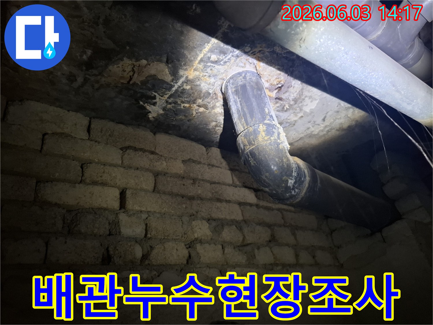 낡은 배관과-벽돌 벽이 있는-지하 공간에서-누수 발생 지점을-조명으로 비추며-세심하게 살펴보는 모습