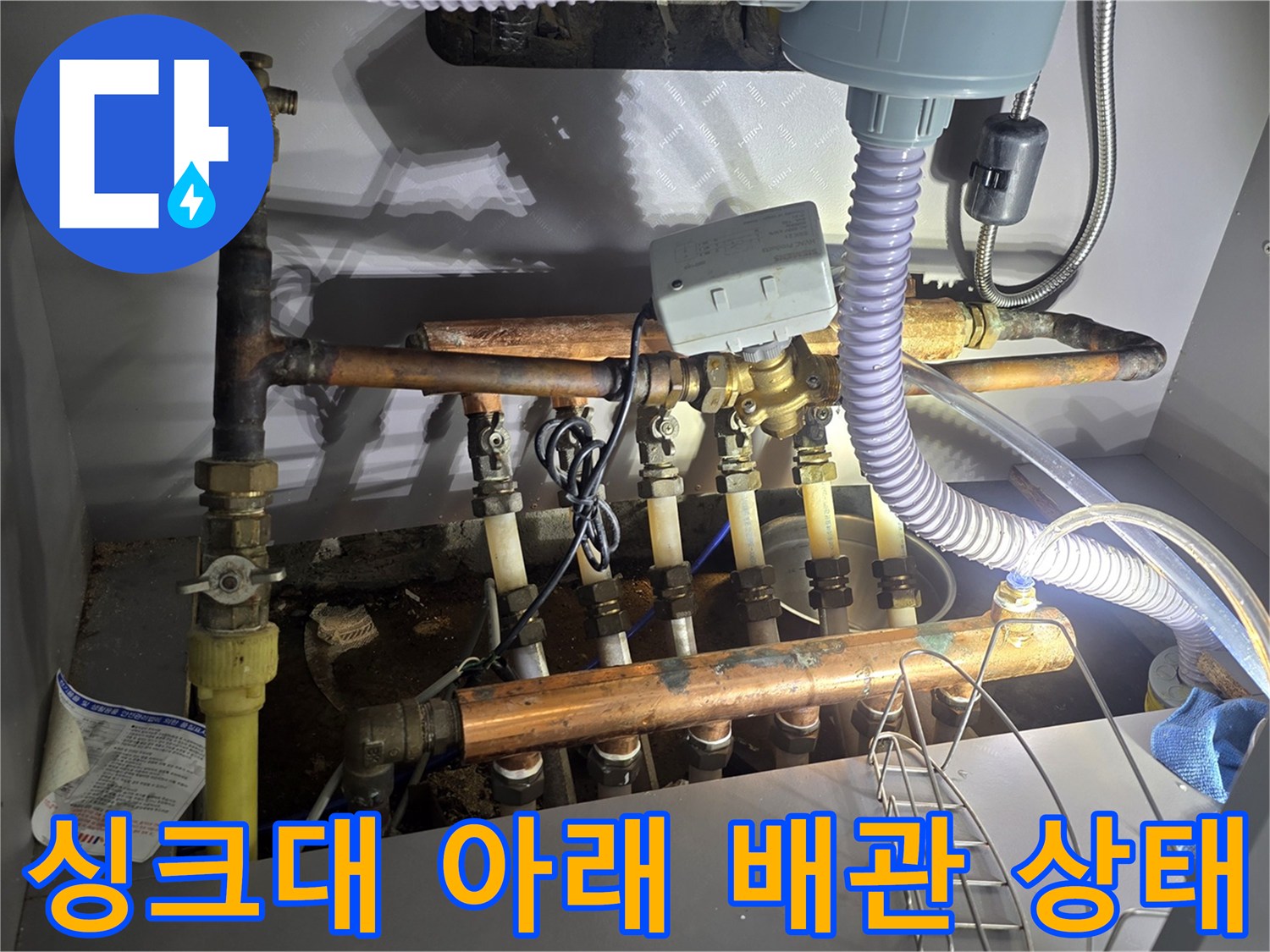 주방 싱크대 하부의 복잡한 보일러 분배기 및 수도 배관 구조물