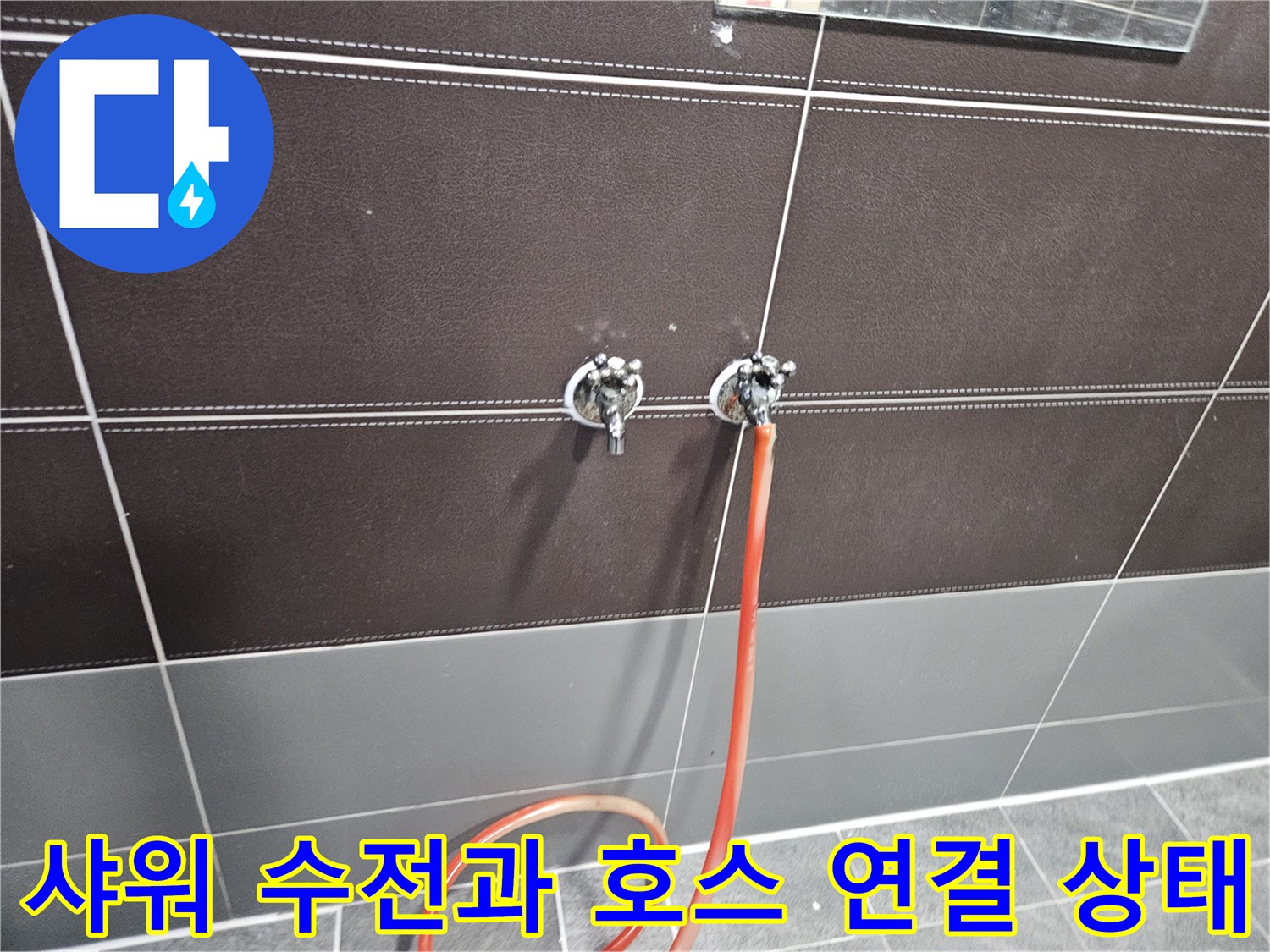 짙은색 타일 벽면에 설치된 샤워 수전과 연결된 호스의 모습입니다.