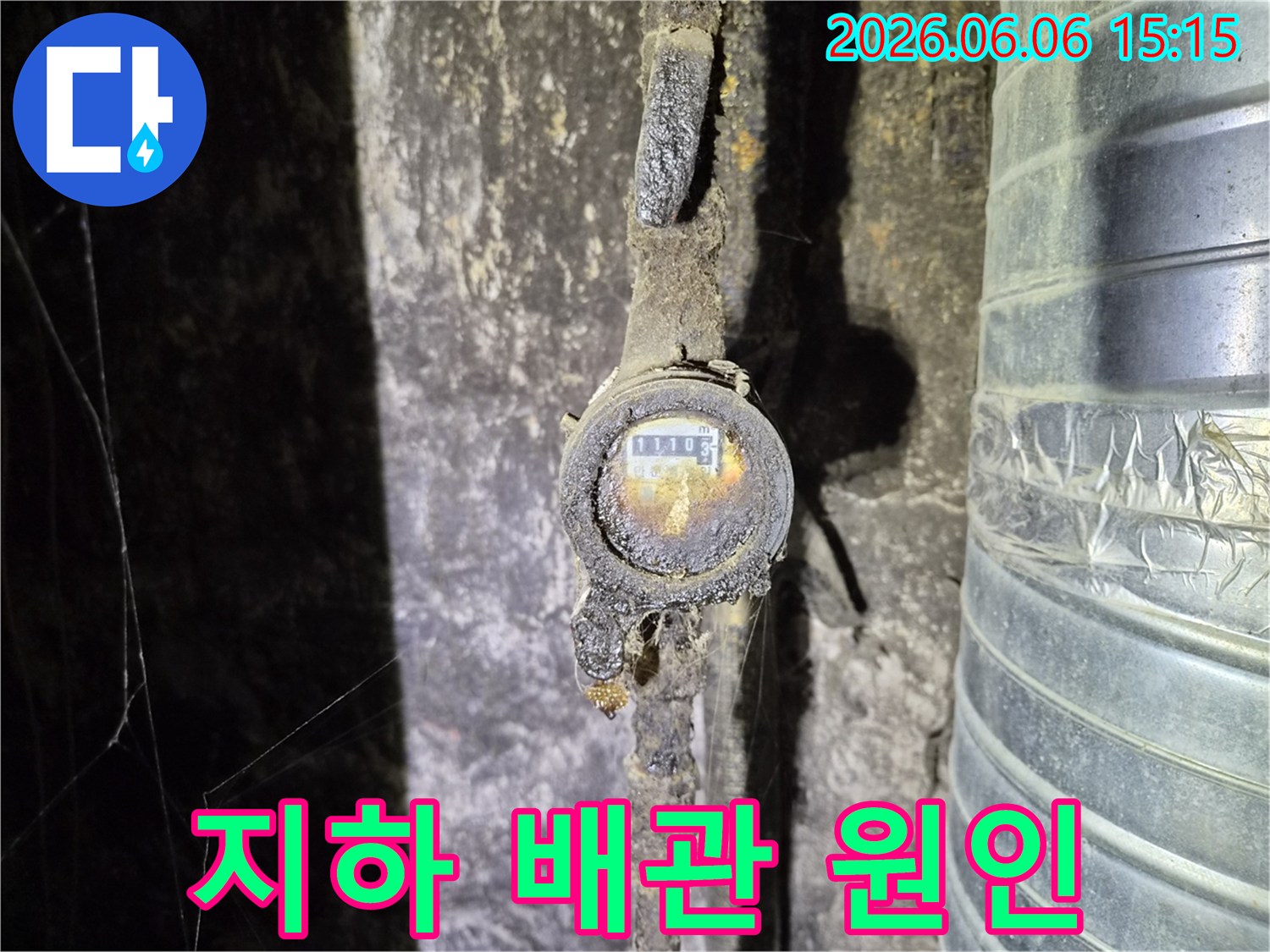 어둡고 습한 지하 공간에서 발견된-오래된 수도 계량기와 심하게 부식된 배관으로-누수 발생의 직접적인 원인을 보여줍니다