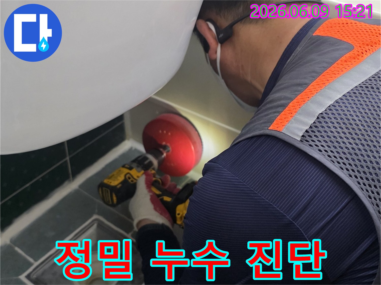 안전-조끼를-입은-엔지니어가-전동-드릴을-사용하여-욕실-배수구-주변을-점검하는-모습