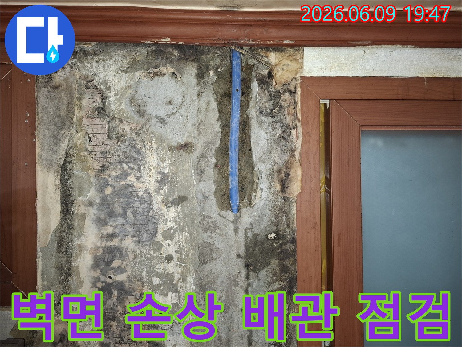 수도배관-누수로-인해-벽면이-심하게-손상되고-배관이-노출된-현장을-점검하는-사진