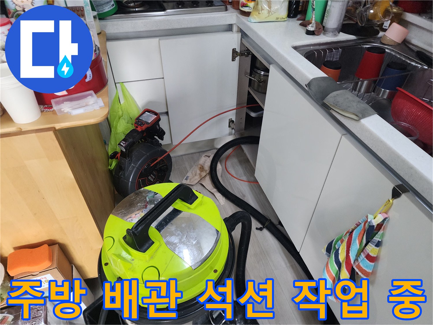 싱크대 밑 배관의 막힌 부분을 뚫기 위해 석션 장비를 사용하는 모습입니다.