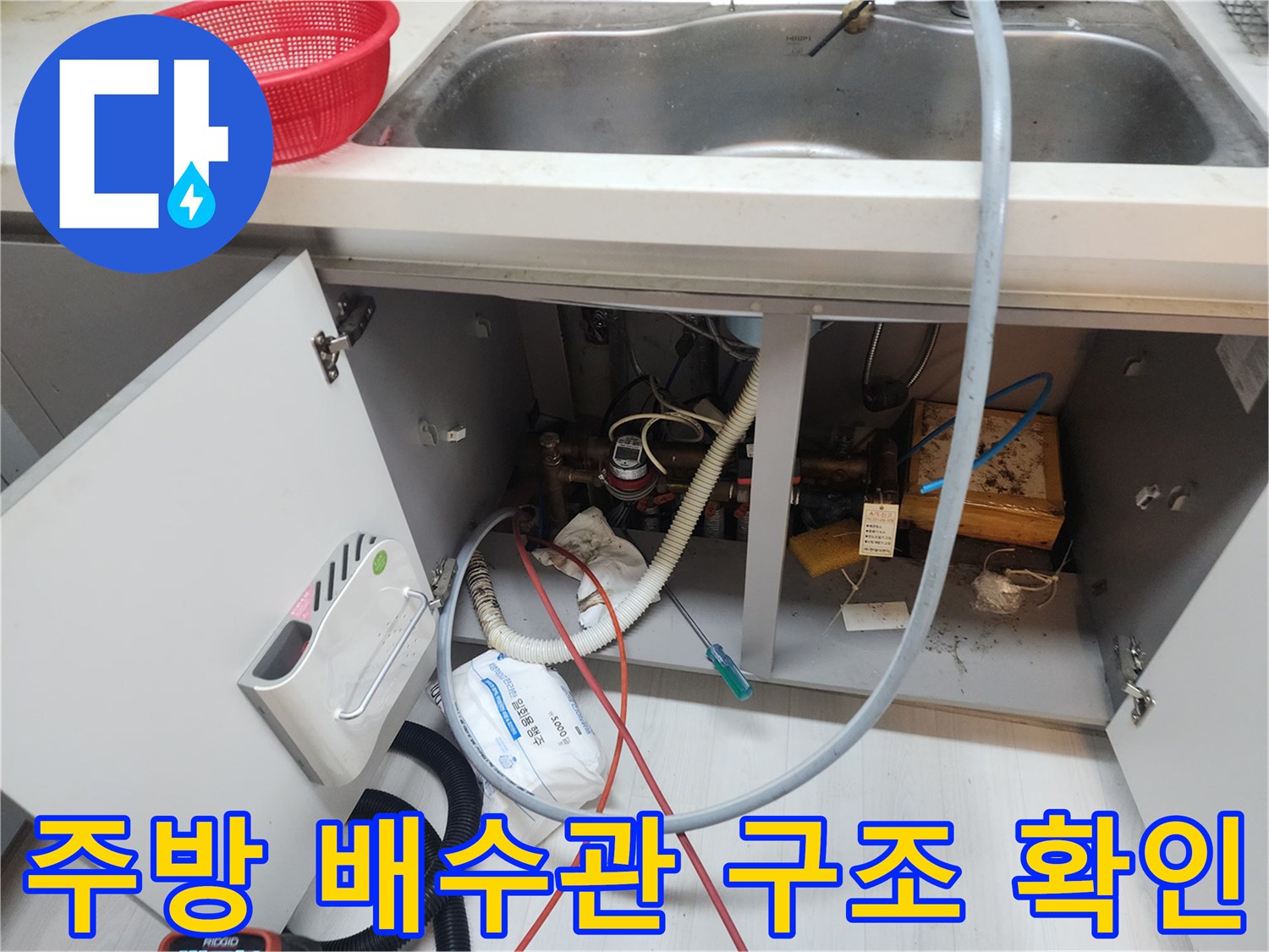 싱크대 하단 배관의 복잡한 연결 부위와 작업 도구들