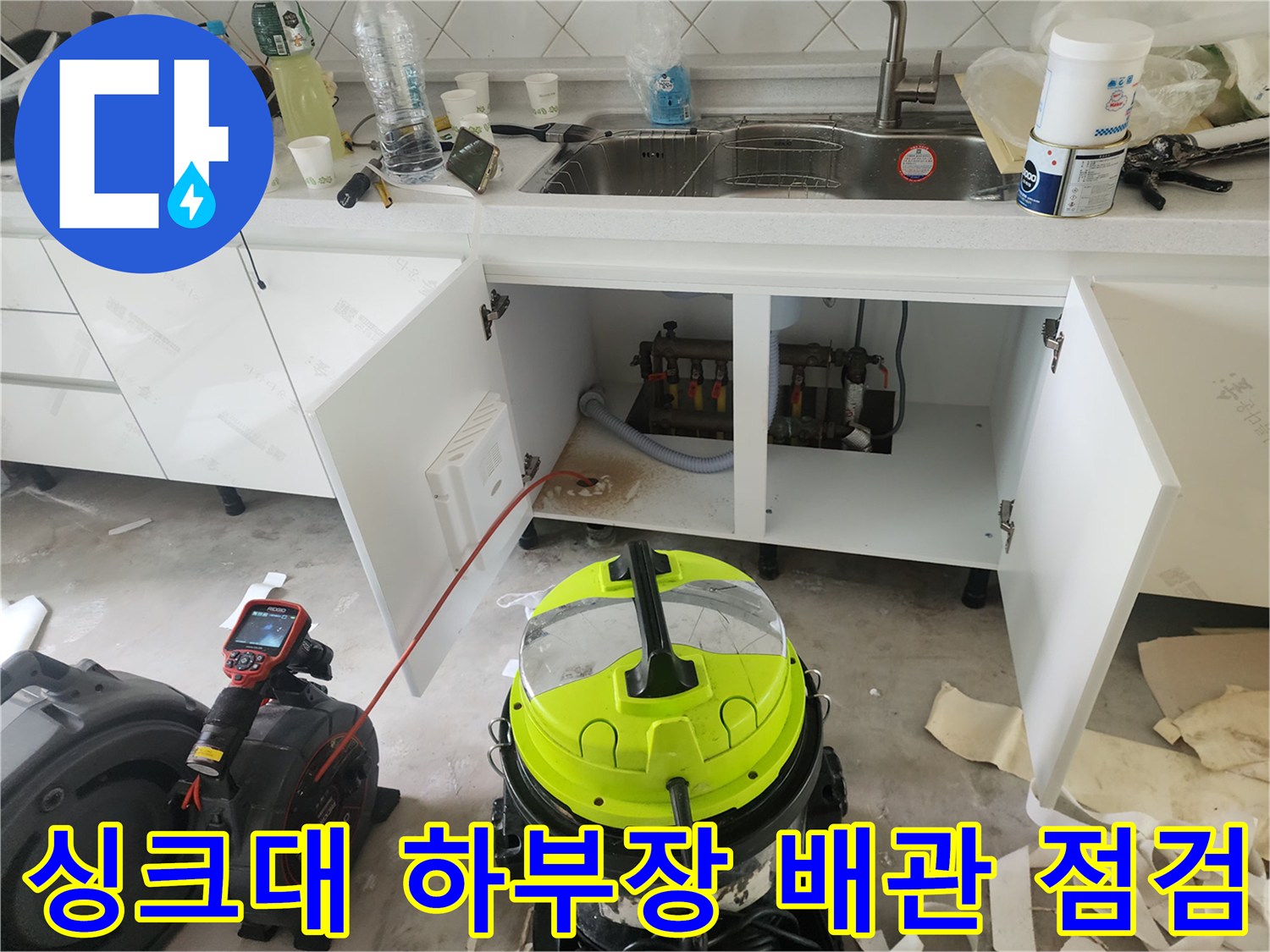 싱크대 하부장 내부의 노출된 배관과 청소 장비를 촬영한 사진
