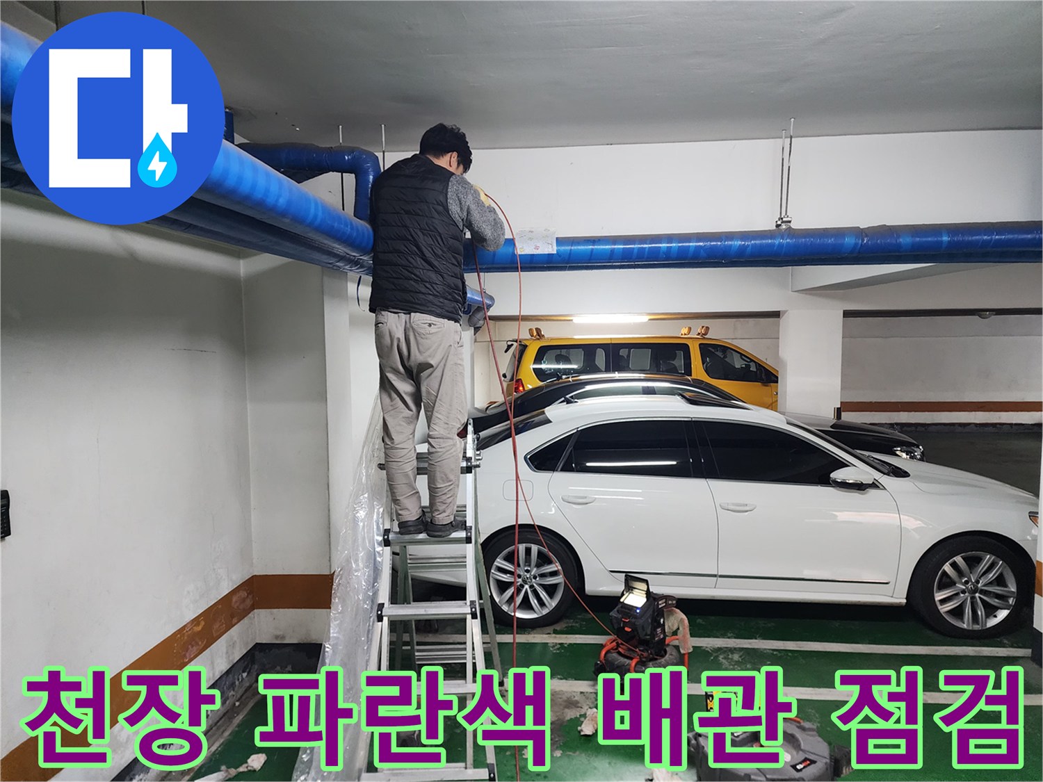 지하주차장 천장에 설치된 굵은 파란색 배관과 작업자