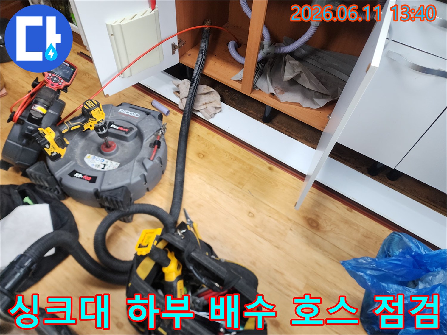 싱크대 밑으로 연결된 굵은 배관과 청소 장비를 보여줍니다.