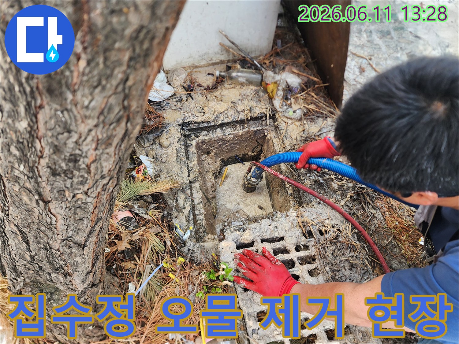 파란색 호스와 붉은 장갑을 착용한 작업자가 집수정을 청소하고 있습니다.