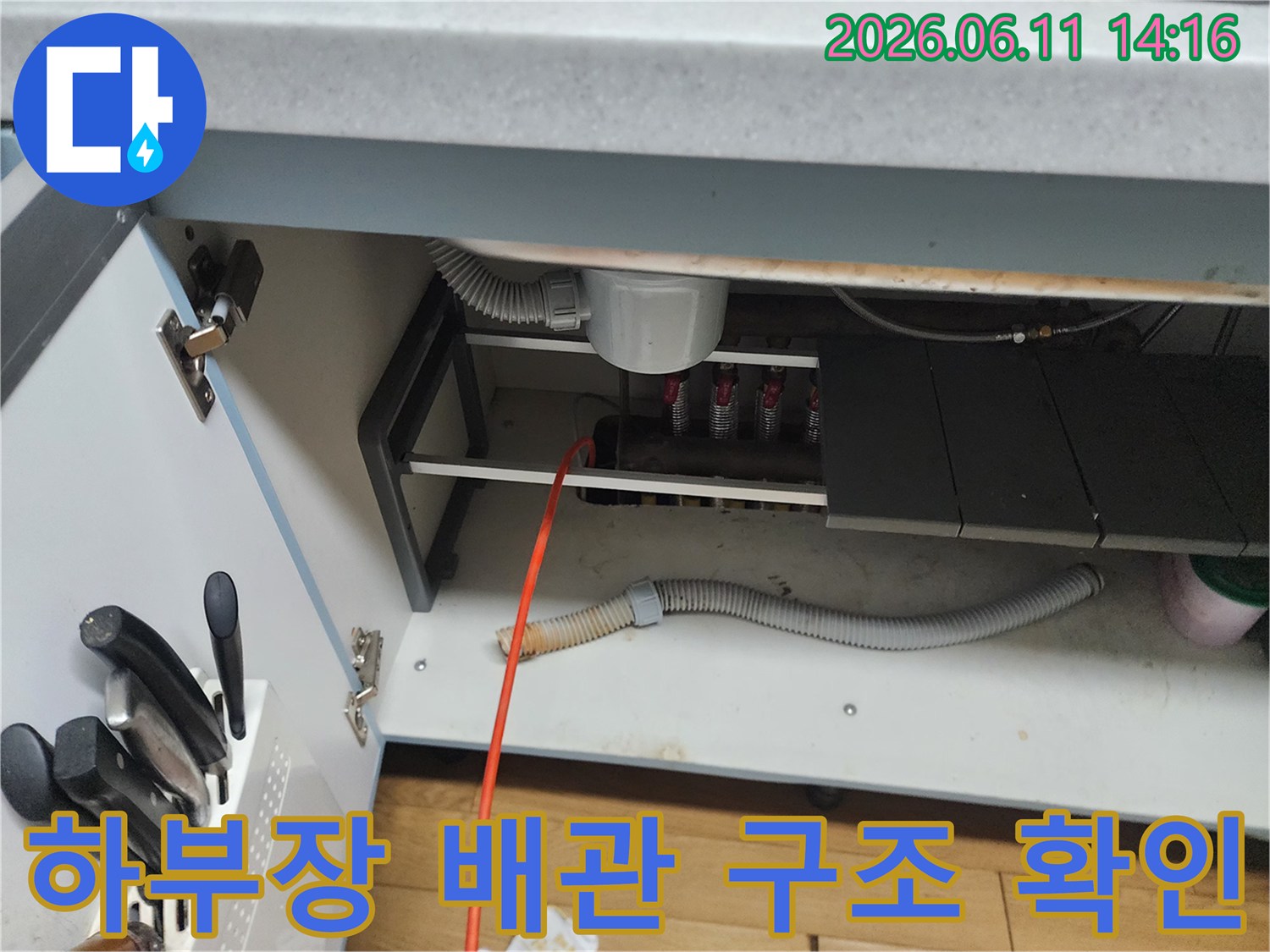 싱크대 아래쪽의 복잡한 배수관 연결 부위와 호스들을 촬영한 모습입니다.
