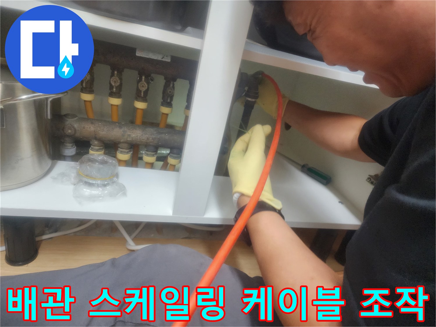 노란색 장갑을 착용한 작업자가 붉은색 케이블을 배관에 넣고 있는 모습