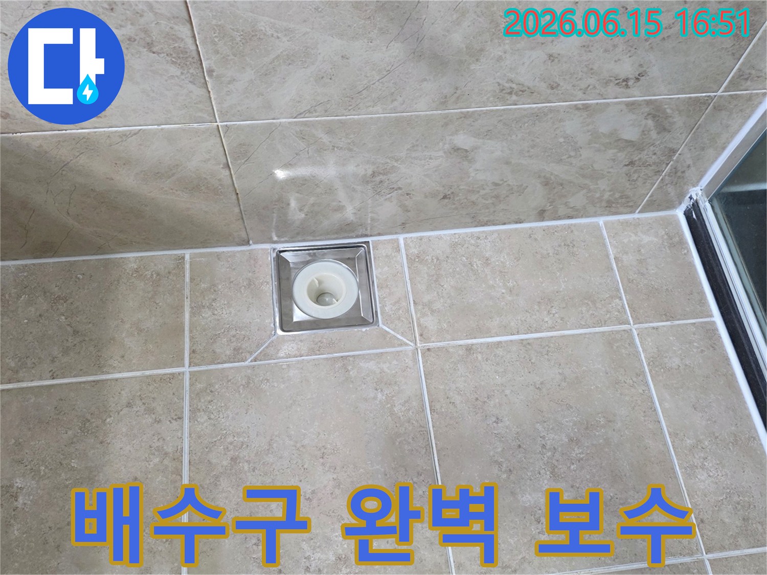 베이지색 타일 바닥에 설치된-금속 사각 배수구의 모습으로-주변 타일과 줄눈의 마감 상태를 보여줍니다