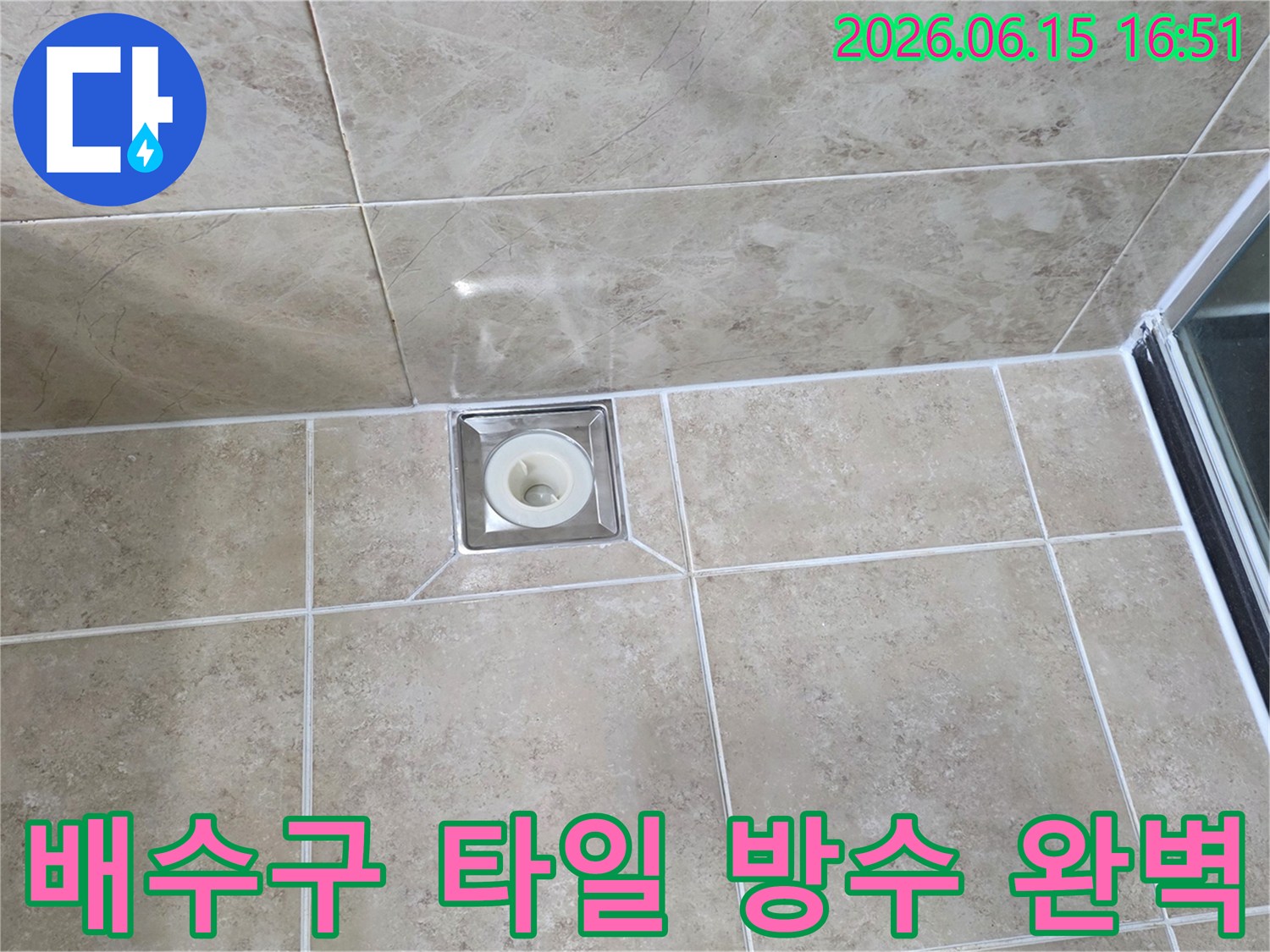 베이지색 타일 바닥에 위치한-사각형 금속 배수구의 모습으로-주변 타일의 접합부와-줄눈의 상태를 상세히 보여줍니다