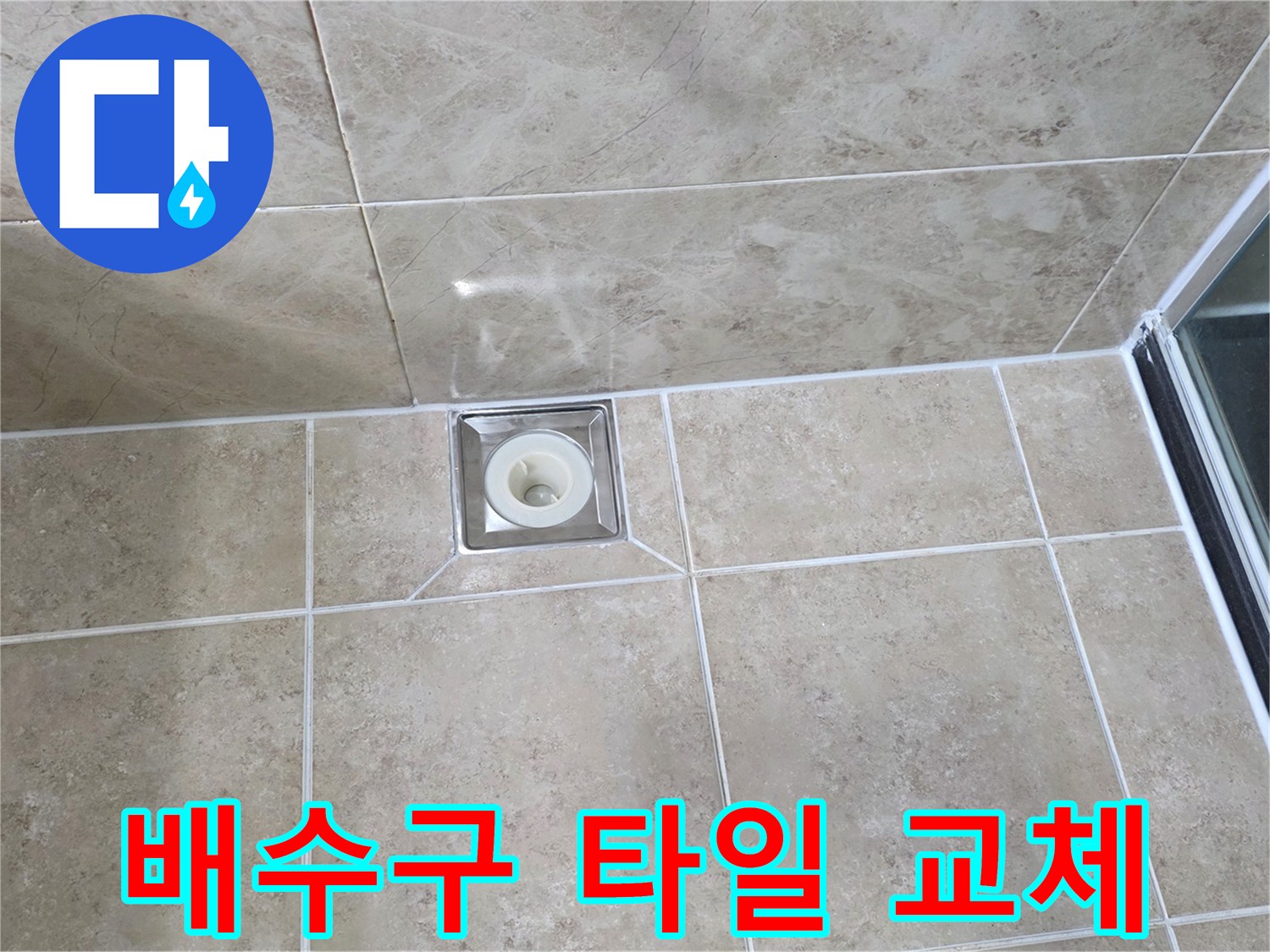 베이지색 타일 바닥에 위치한-사각형 금속 배수구의 모습으로-주변 타일의 접합부와-줄눈의 상태를 상세히 보여줍니다