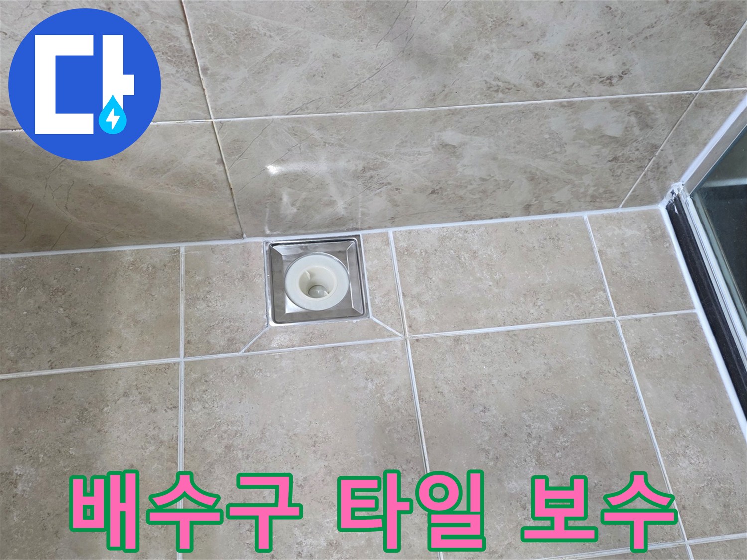 베이지색 타일 바닥에 위치한-사각형 금속 배수구의 모습으로-주변 타일의 접합부와-줄눈의 상태를 상세히 보여줍니다