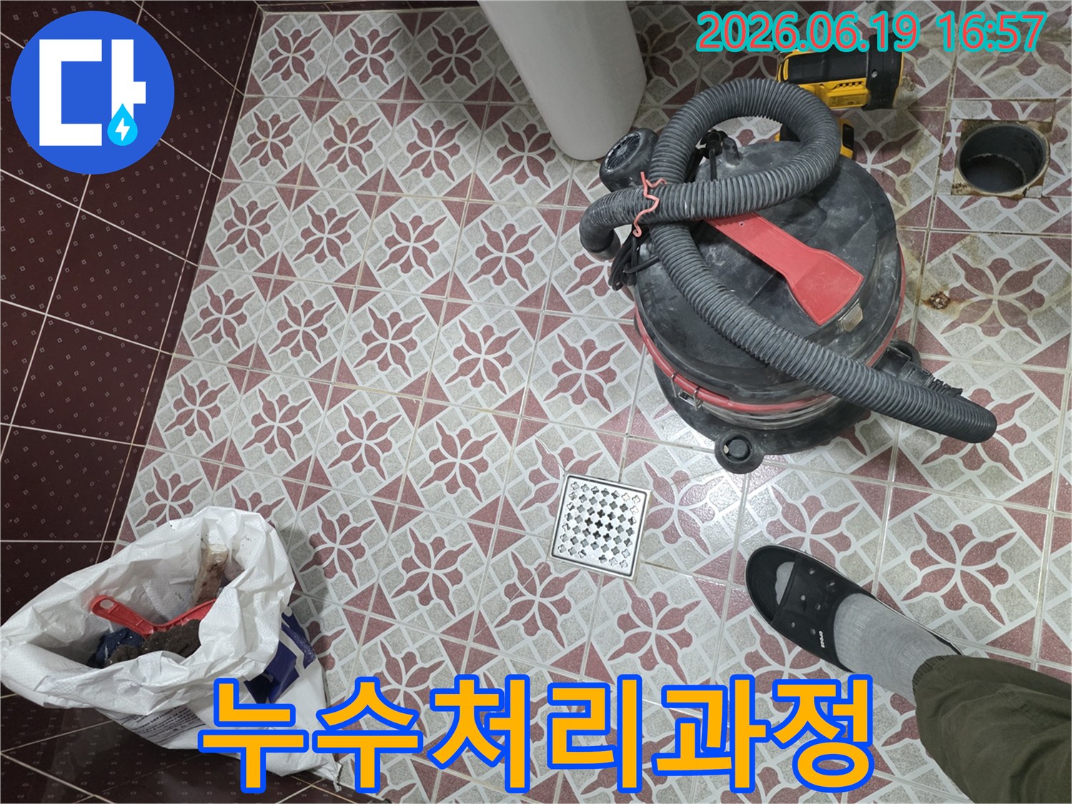화장실 배수구 주변의-누수 처리 과정-습식 청소기로 물을 제거하고-정리된 바닥의 모습-작업자의 발과 함께