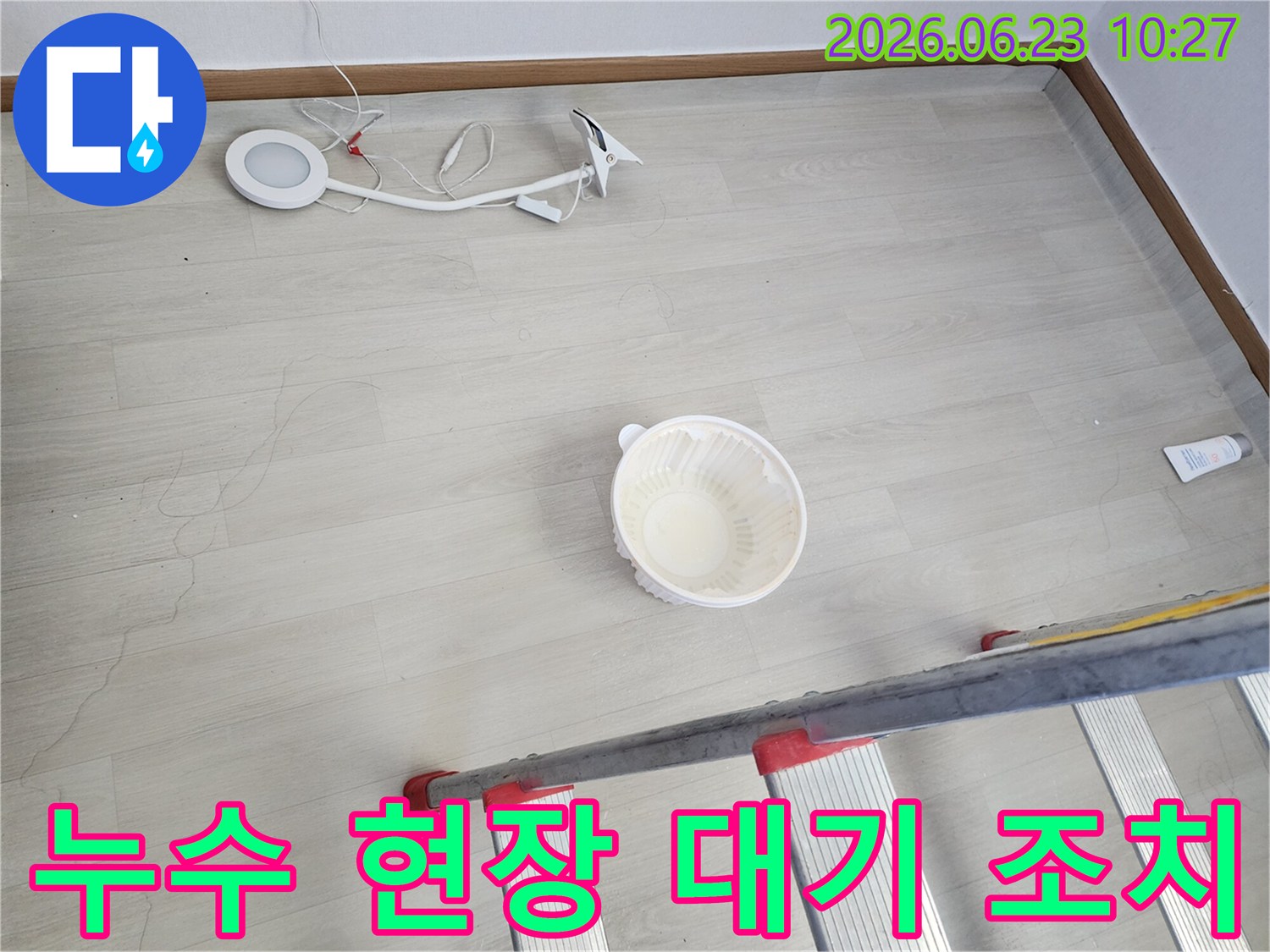 누수로 인해 바닥에 물이 떨어지는 것을 임시로 모으는 그릇과-작업을 위한 사다리-조명 장비가 바닥에 놓여 있는-누수 공사 전 현장 모습입니다