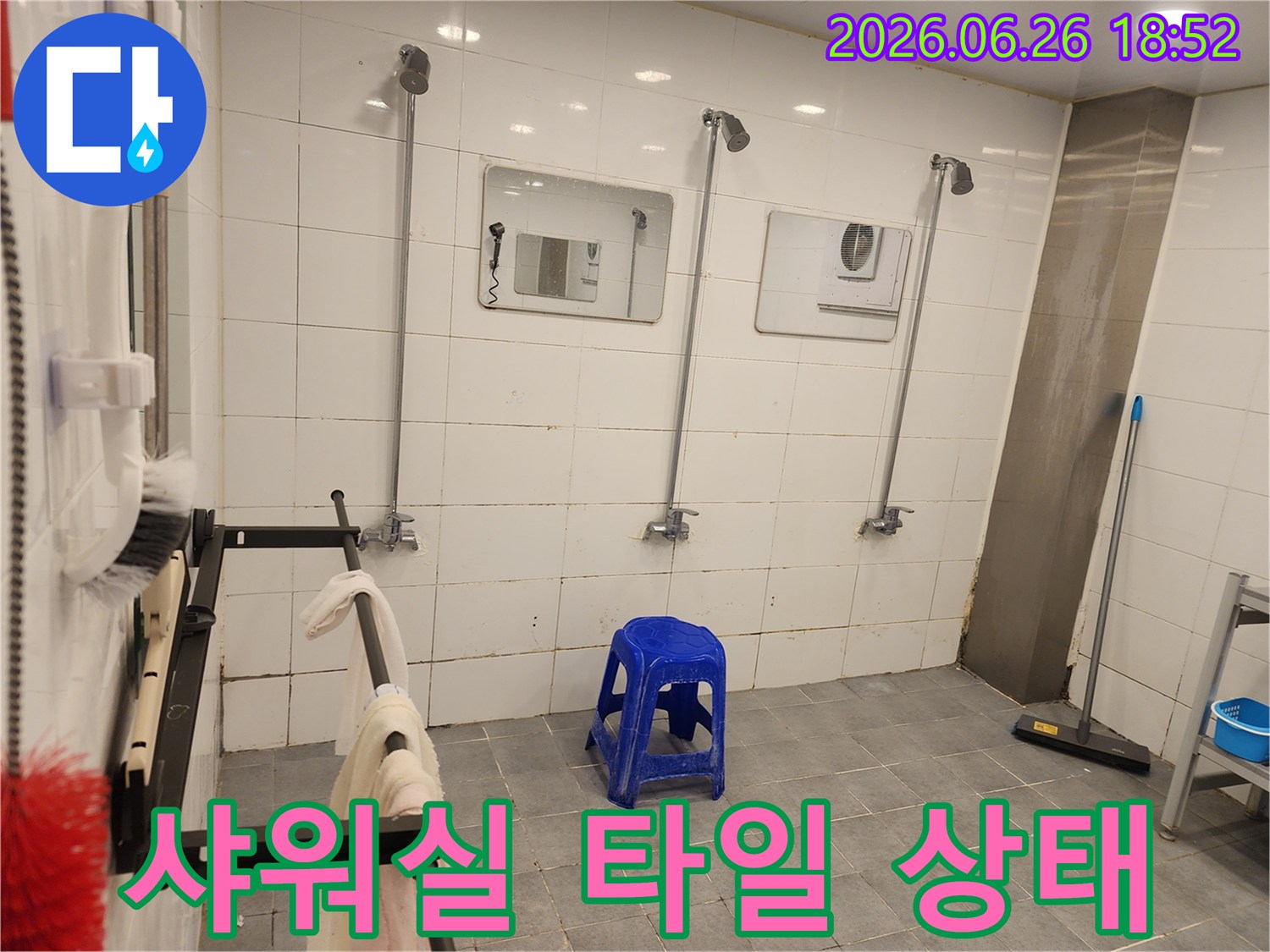 오래된 샤워실의-타일 벽면과-여러 개의-샤워 헤드-그리고-중앙에 놓인-파란색 의자
