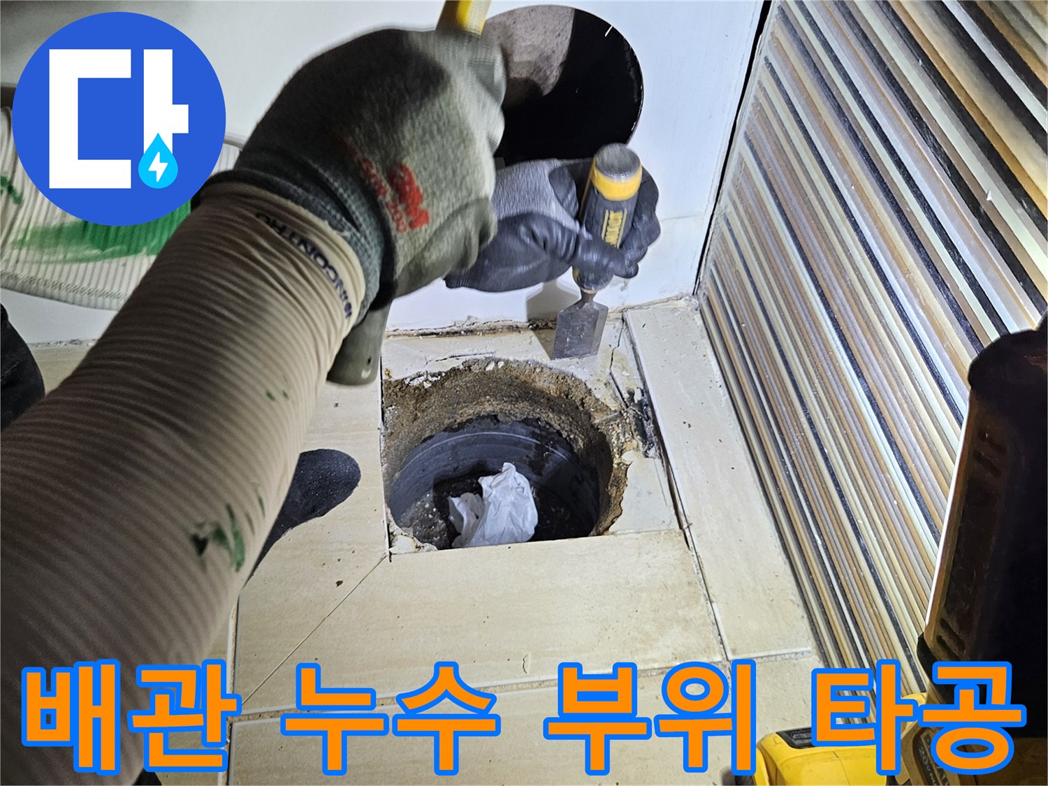드릴을 사용하여 욕조 하단부의 배관 결함을 찾기 위해 타일 구멍을 내는 장면입니다.