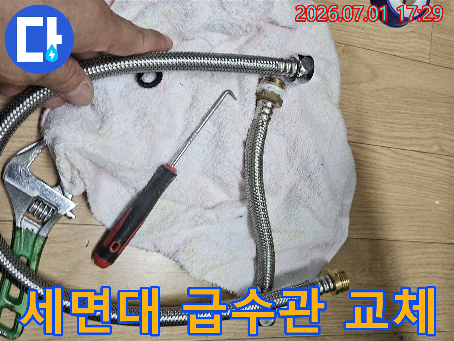 이 사진은 세면대 급수관 교체 작업을 위해-새로운 호스와 공구를 준비하는 장면입니다