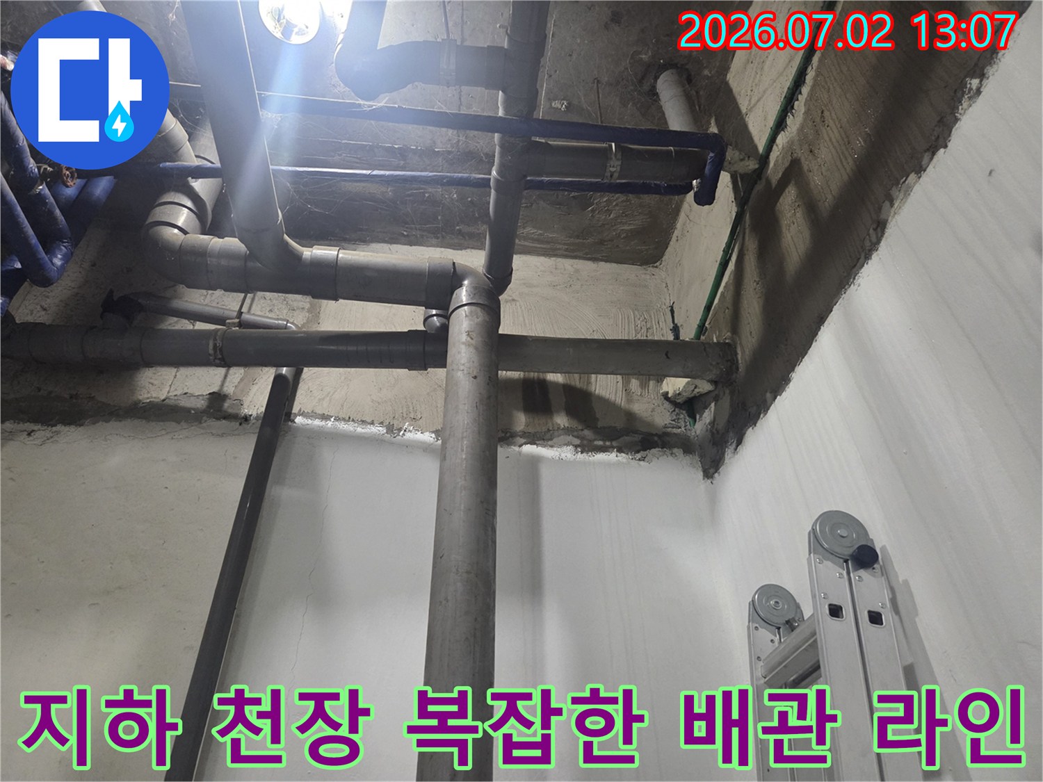 지하 공간의 천장과 벽면을 따라 설치된 복잡한 회색 하수 배관 시스템